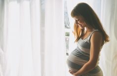 Young beautiful pregnant woman standing near window at home