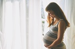 Young beautiful pregnant woman standing near window at home