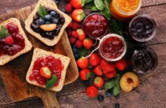 Sandwiches with plum, strawberry jam and fresh fruits on wooden background.