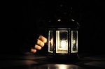 Fingers illuminated wirt light from candle lantern in dark, black background with soft fire